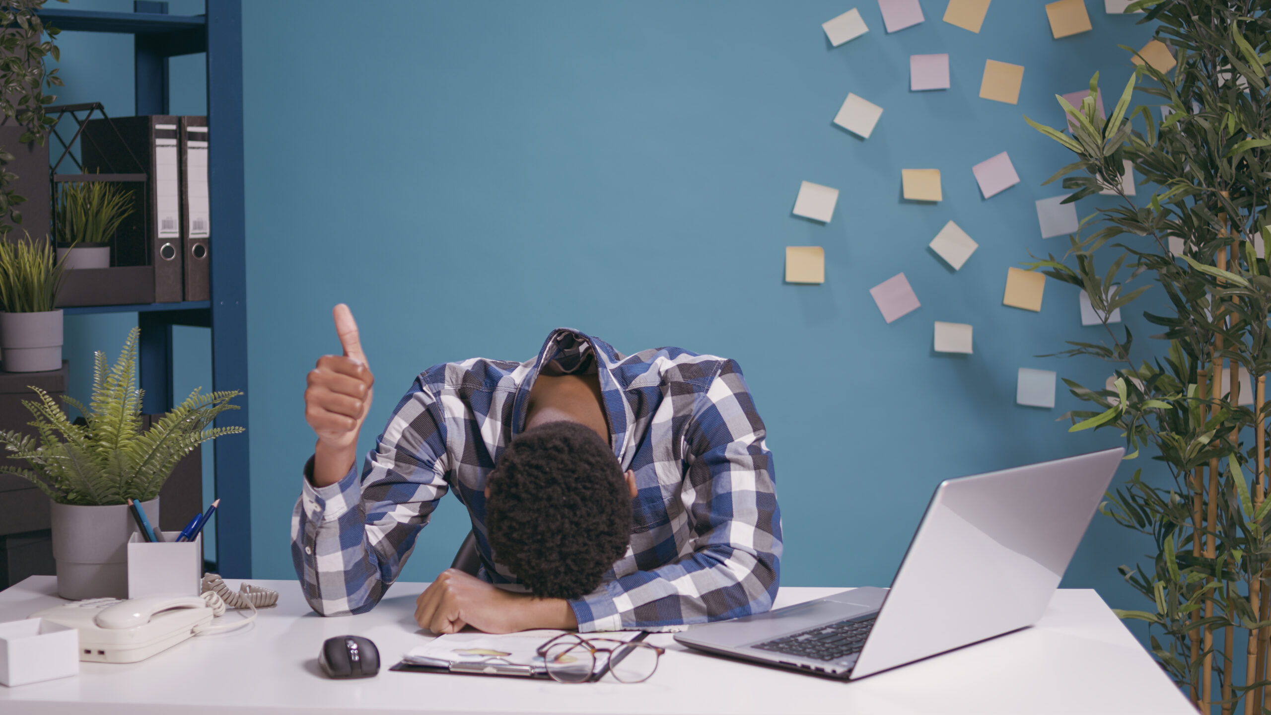 Exhausted worker putting head on desk and showing thumbs up sign